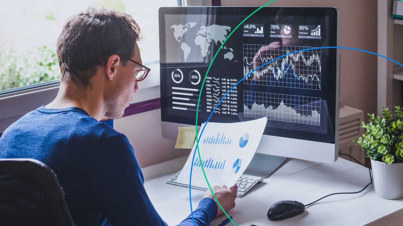 A trader analysing charts and financial data on a computer screen, holding a printed report with graphs, representing 16 effective day trading strategies for beginners.
