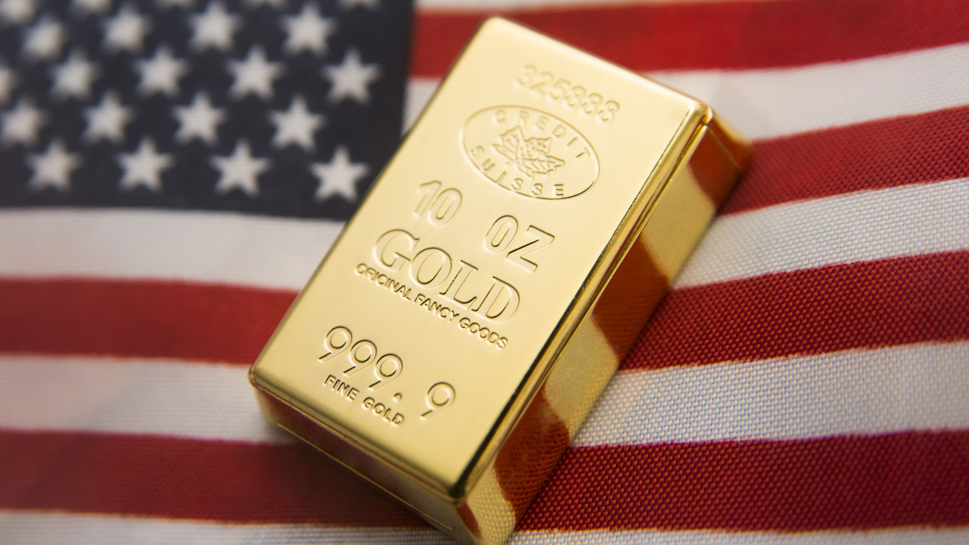 A 10-ounce gold bar resting on the American flag, representing the impact of Non-Farm Payroll (NFP) data on the price of gold.