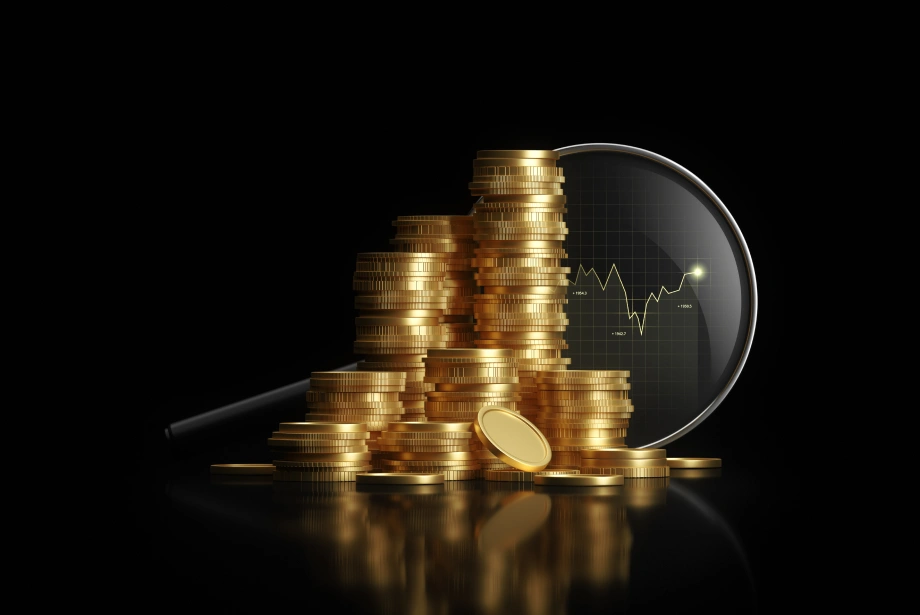 Stacks of gold coins on a black reflective surface with a magnifying glass showing a financial chart, symbolizing wealth and market analysis